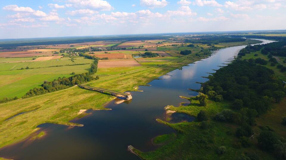 A river with a bridge, surrounded by fields and forests.