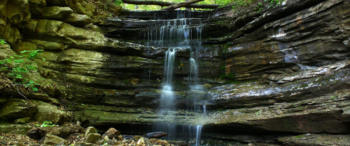 A waterfall cascading down a rocky cliff surrounded by greenery.