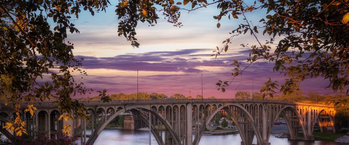 A stone bridge over a river at dusk with a sunset sky.