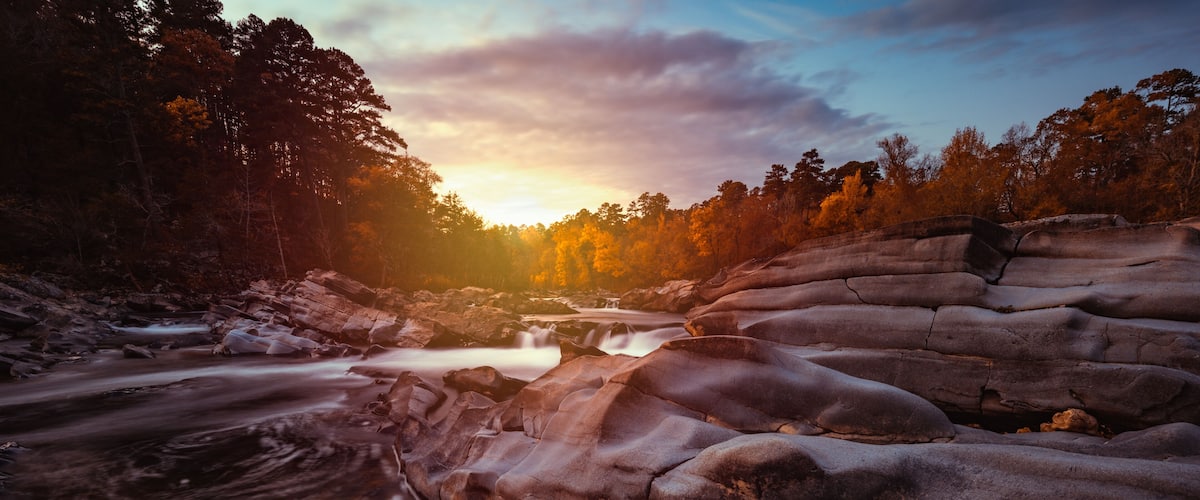 A river flowing through a rocky landscape with a sunset in the background.