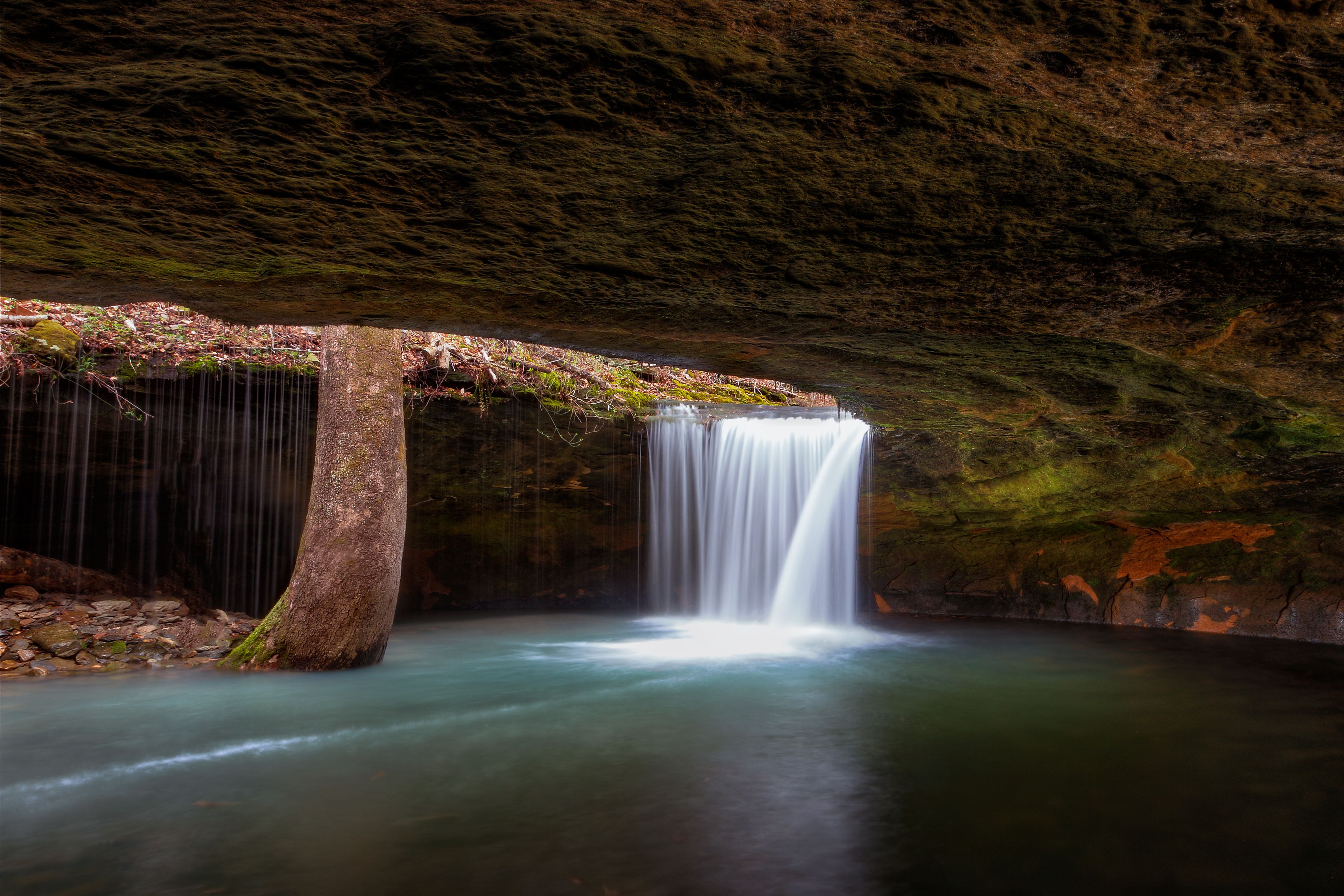 Una cascada que cae sobre rocas cubiertas de musgo hacia una poza tranquila.