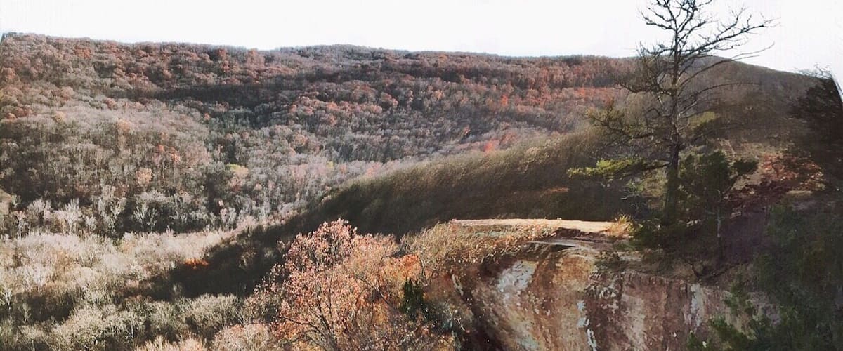 A person sitting on a rock overlooking a cliff with sparse vegetation and a clear sky.
