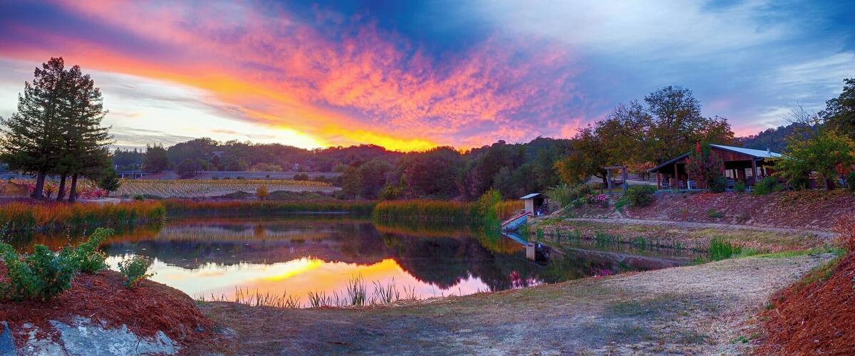 A sunset over a lake with a wooden cabin and trees.