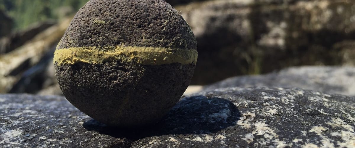A spherical rock with a yellow patch on a rocky surface.