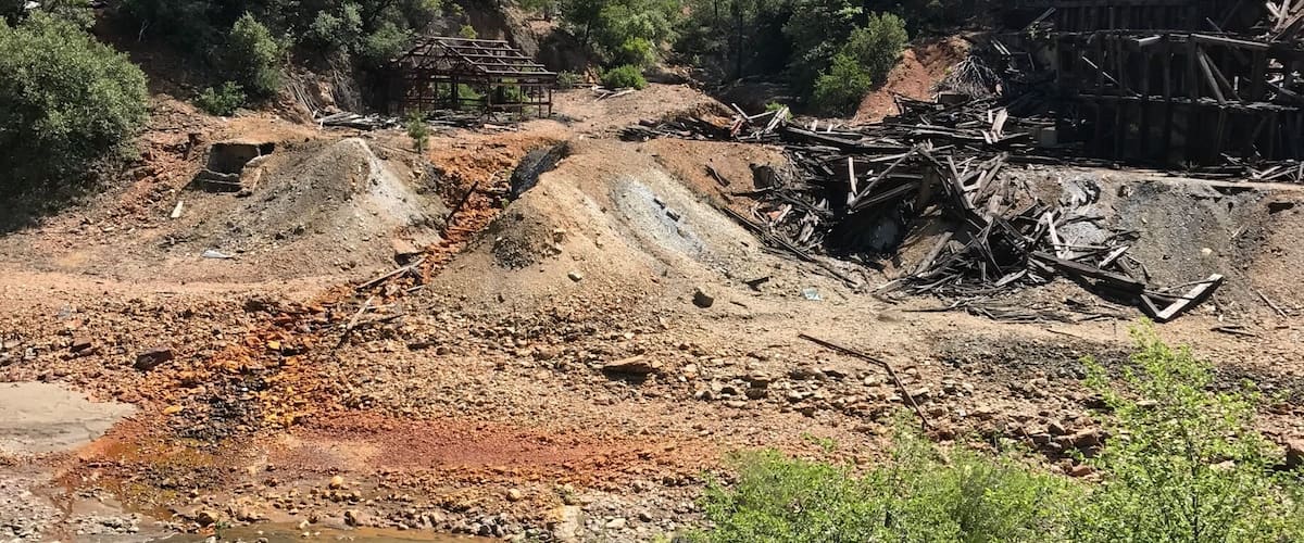 A forested hillside with a river at the base, construction debris, and a clear sky.