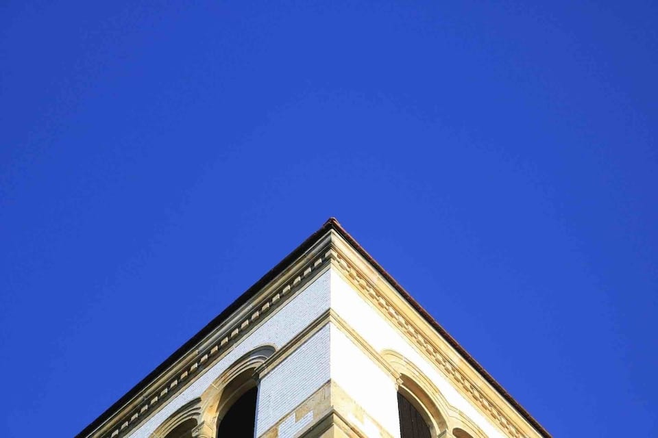 Ein Gebäude mit einer Ecke, die gewölbte Fenster und ein dreieckiges Giebelfeld zum blauen Himmel zeigt.