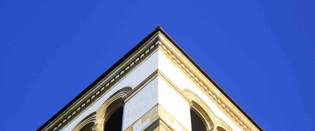 A building with a corner featuring arched windows and a triangular pediment against a clear blue sky.