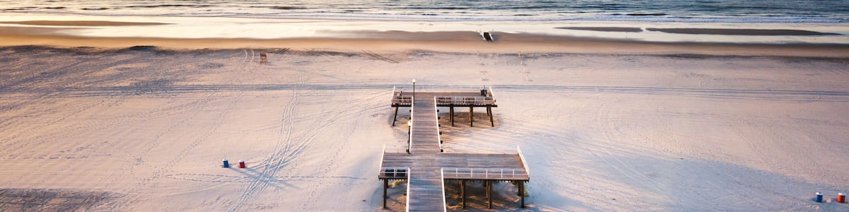 A beach with a wooden pier extending into the ocean, sandy shore, and a clear sky.