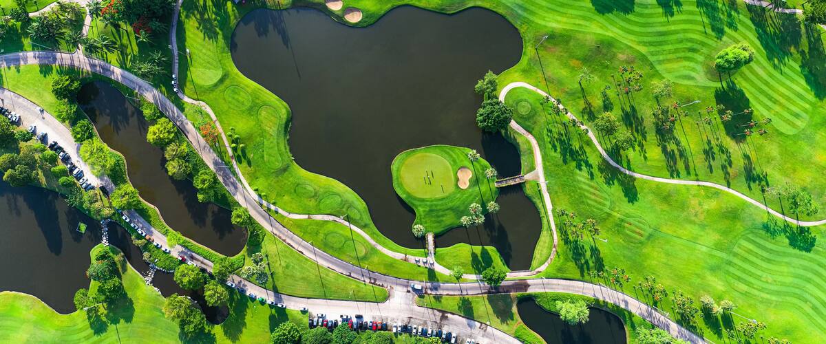 An aerial view of a golf course with multiple ponds, winding roads, and lush green fairways.