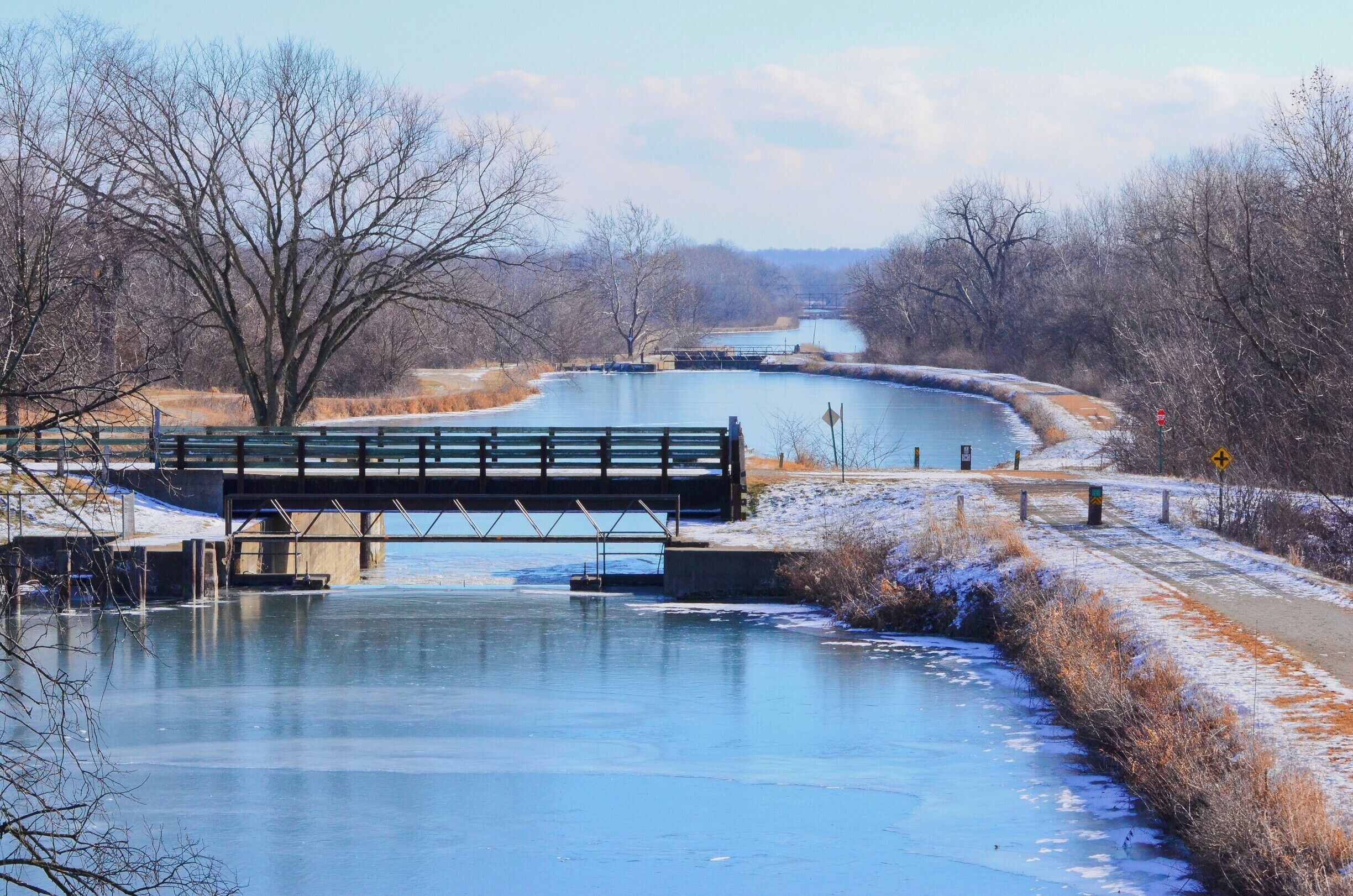 A frozen river with a bridge, surrounded by leafless trees and a clear sky.