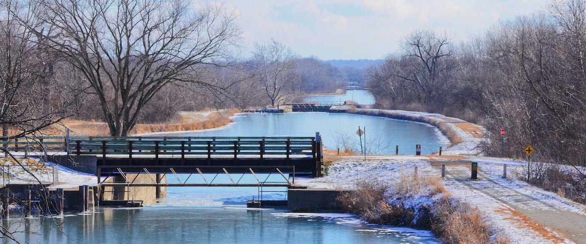 A frozen river with a bridge, surrounded by leafless trees and a clear sky.