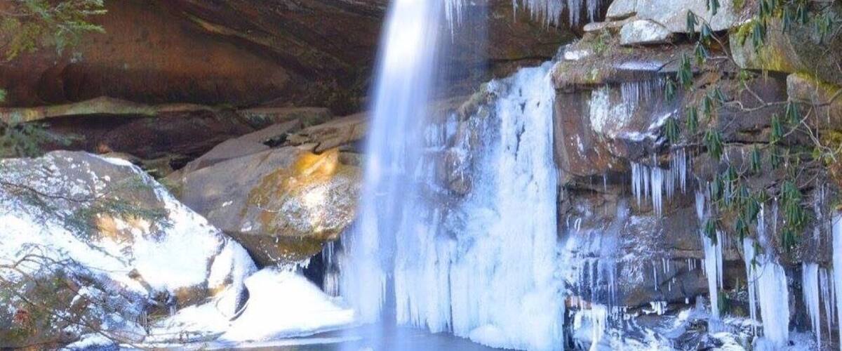 A waterfall cascading over rocks into a clear pool surrounded by snow and ice formations.
