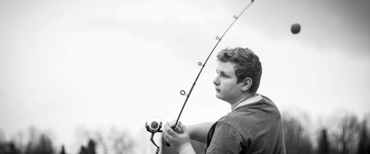 A person holding a fishing rod with a ball in mid-air, likely a fish, in a natural outdoor setting.