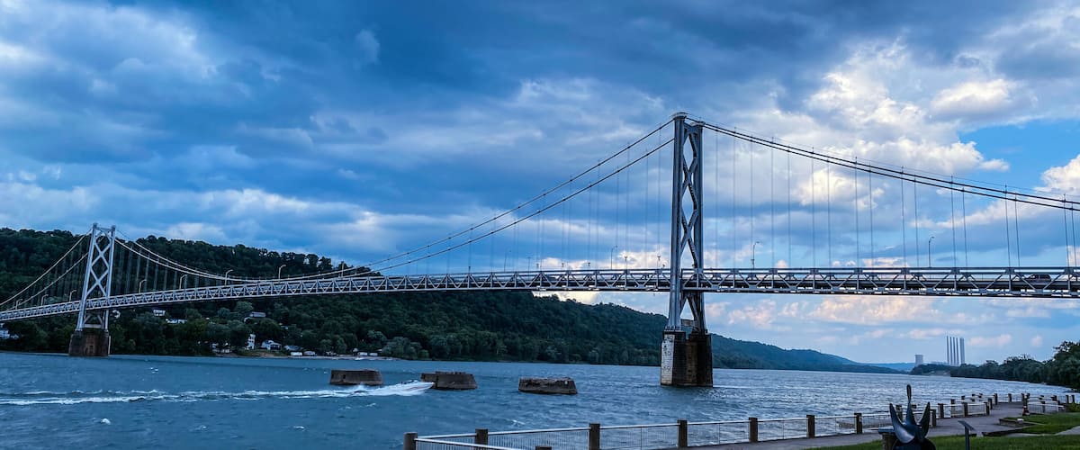 A suspension bridge over a river with a forested hillside in the background.