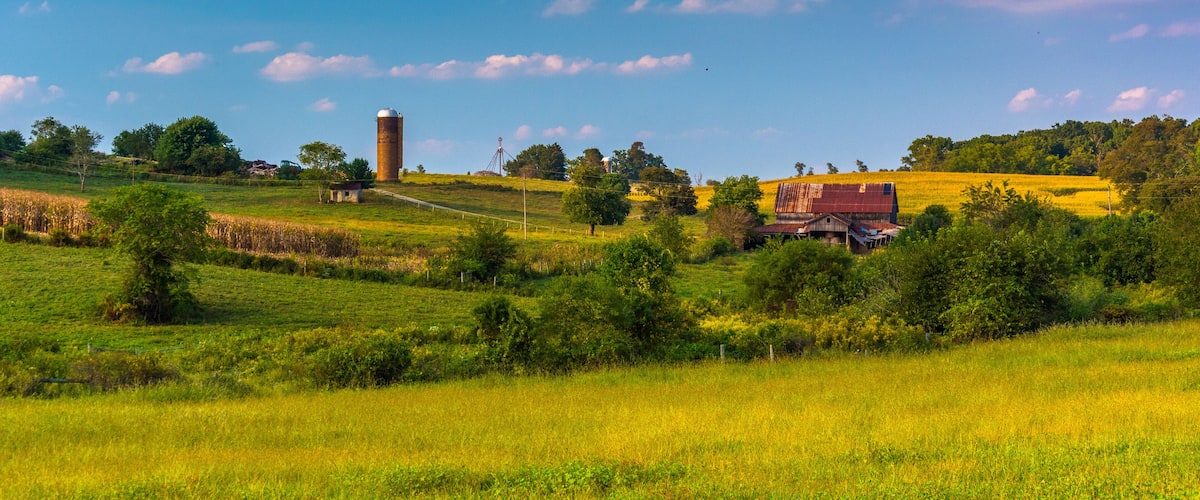 A rural landscape with a silo, barn, and rolling hills.
