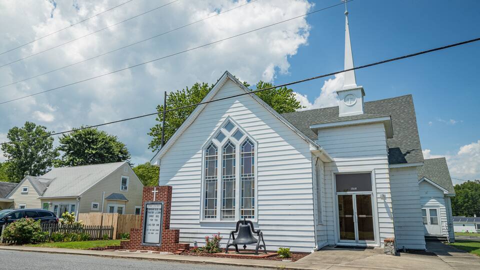 A white church with a steeple, a bell, and a signboard.
