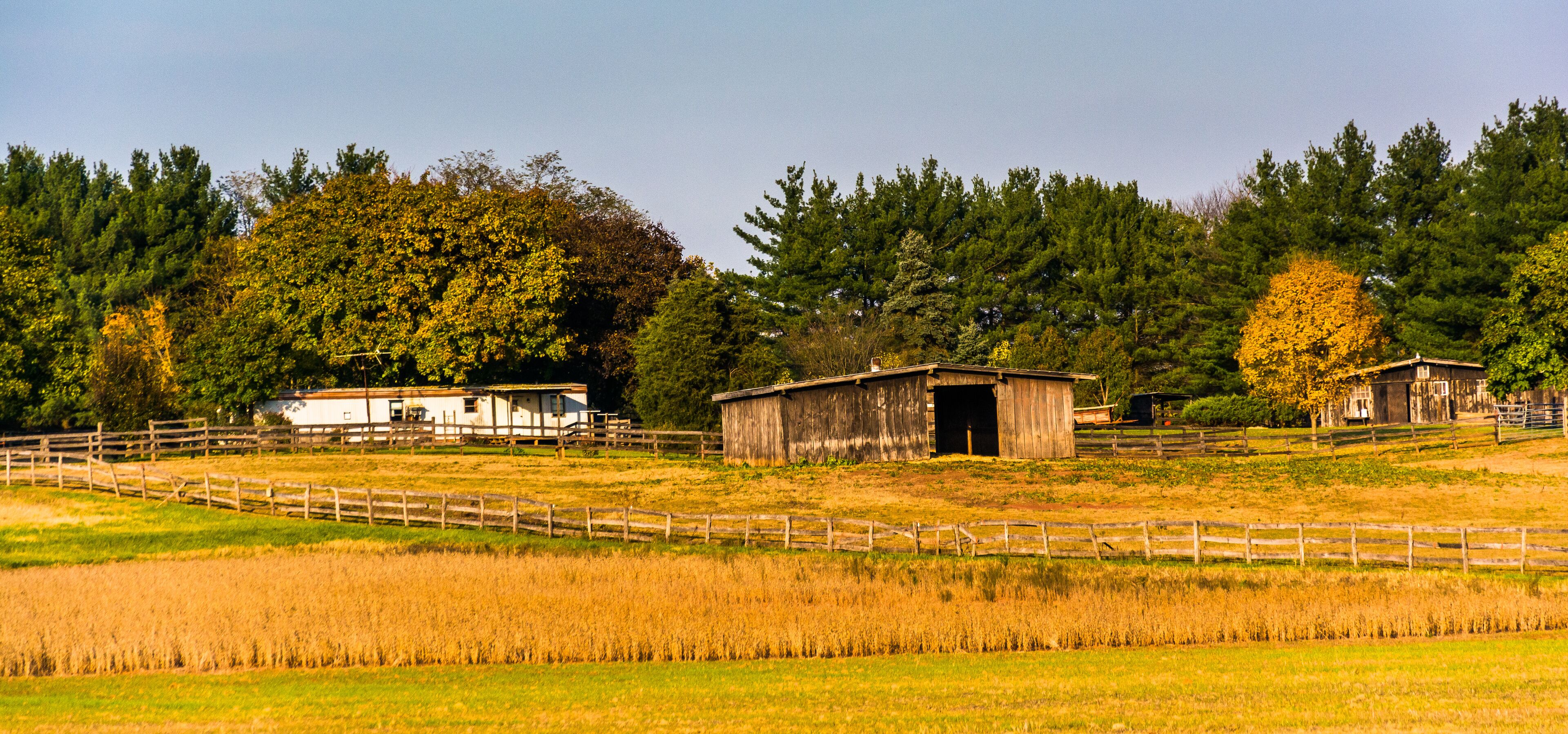 A rural landscape with a barn, a white house, and a fenced field.