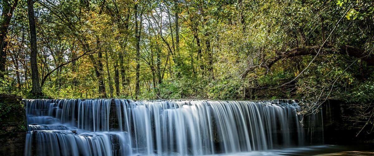 A multi-tiered waterfall surrounded by dense forest.