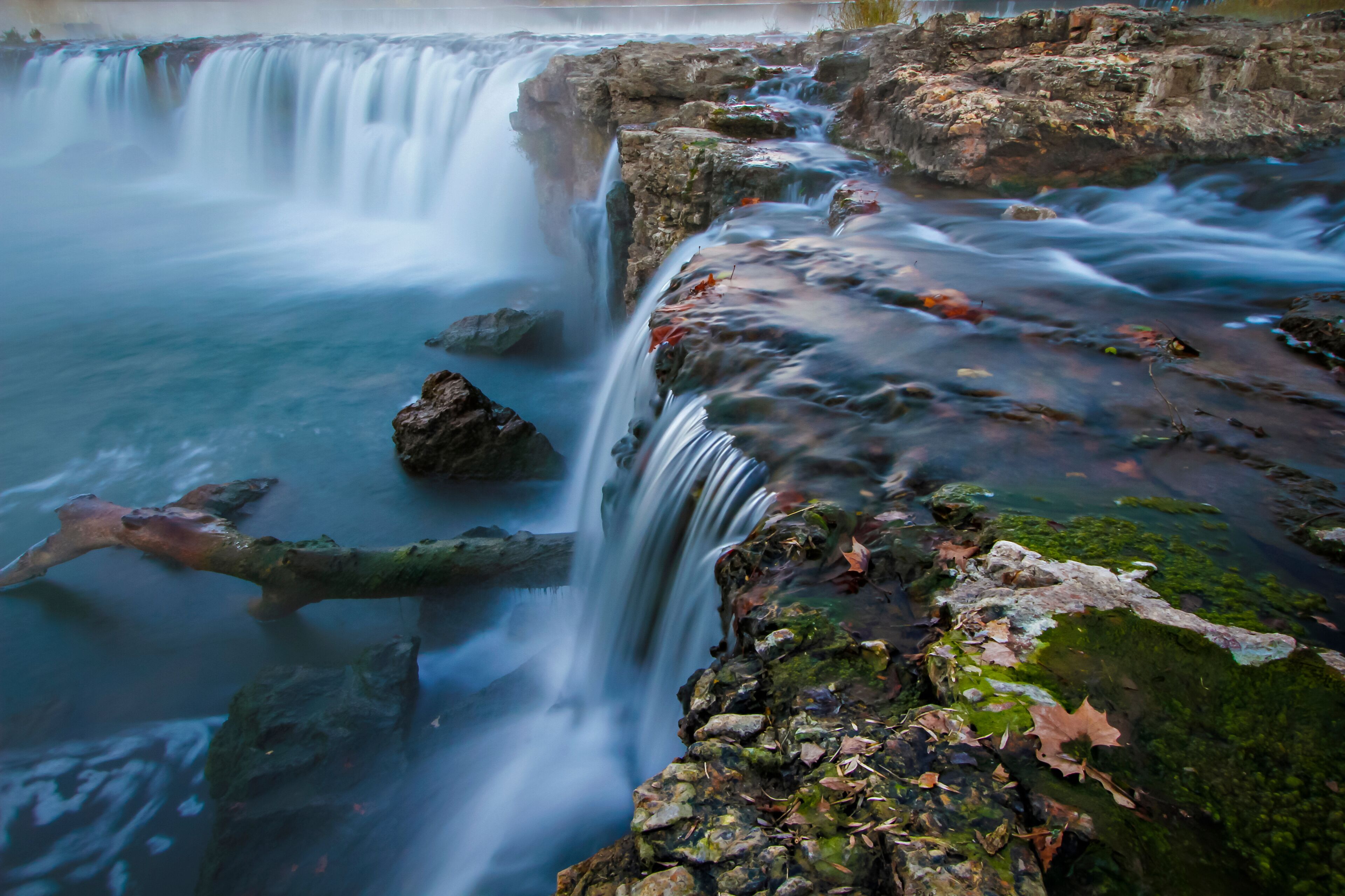 A waterfall cascading over rocks with moss and fallen leaves.