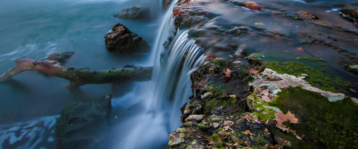 A waterfall cascading over rocks with moss and fallen leaves.