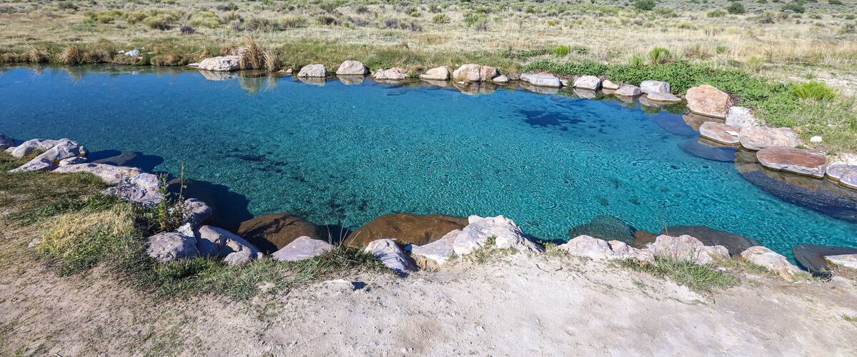 A clear blue pond surrounded by rocks, with a mountain in the background.