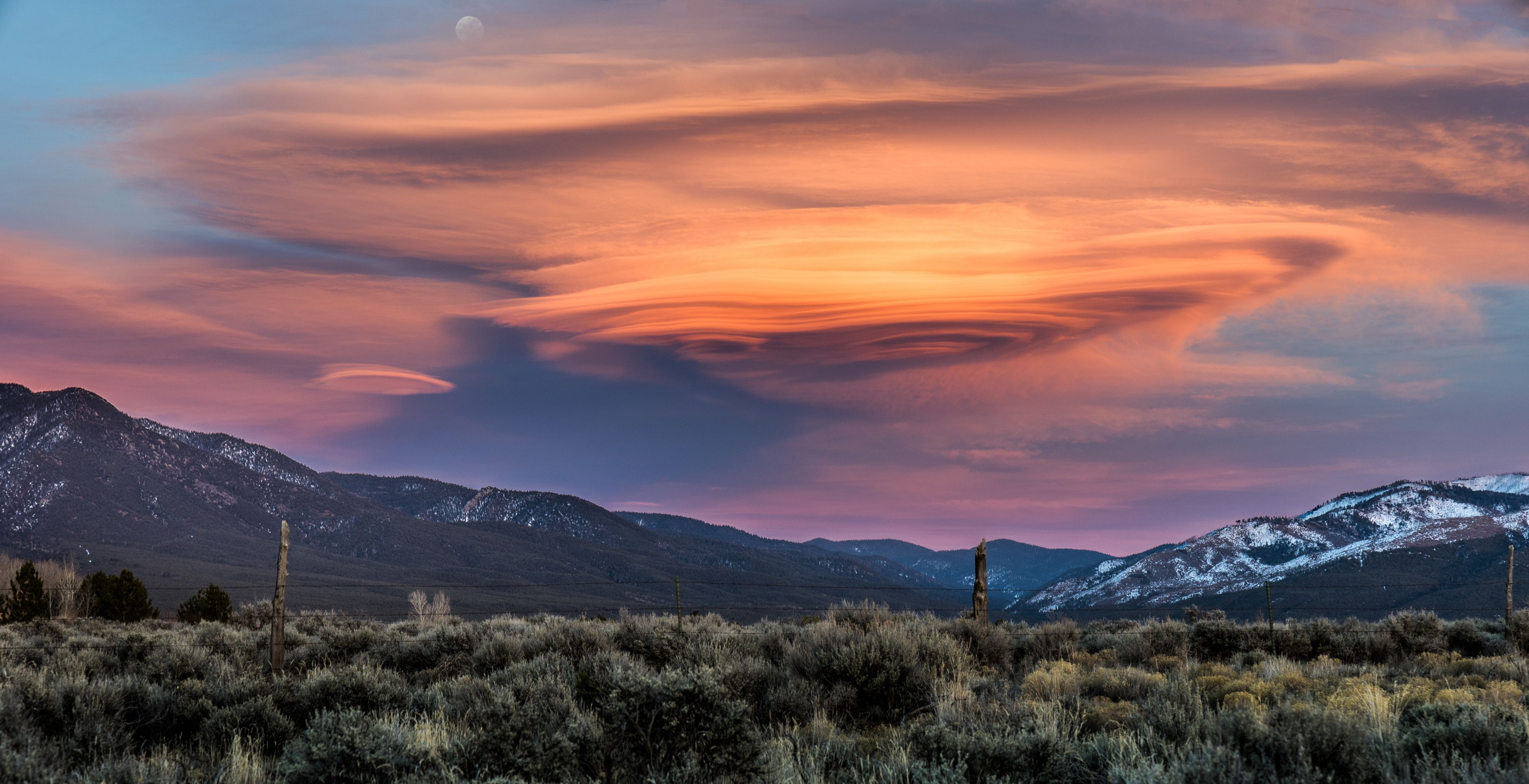 Pôr do sol sobre uma paisagem montanhosa com uma formação de nuvens marcante.