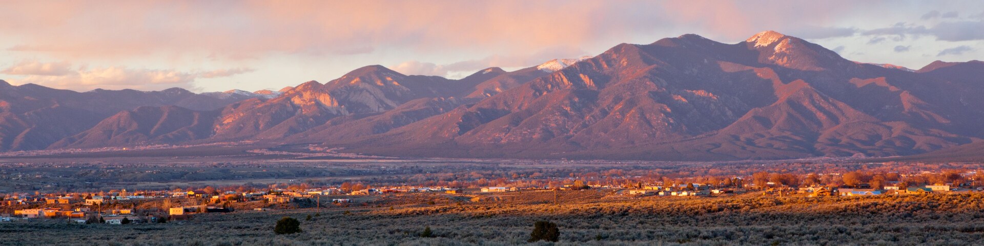 Un paisaje montañoso con un pueblo en primer plano y un cielo al atardecer.