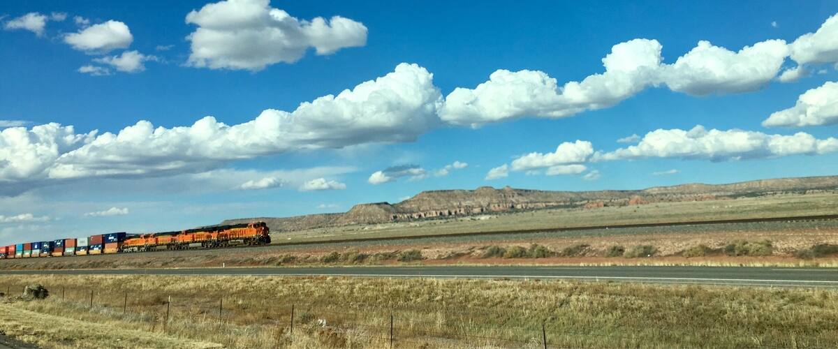 A train on a railway track with a clear blue sky and scattered clouds.