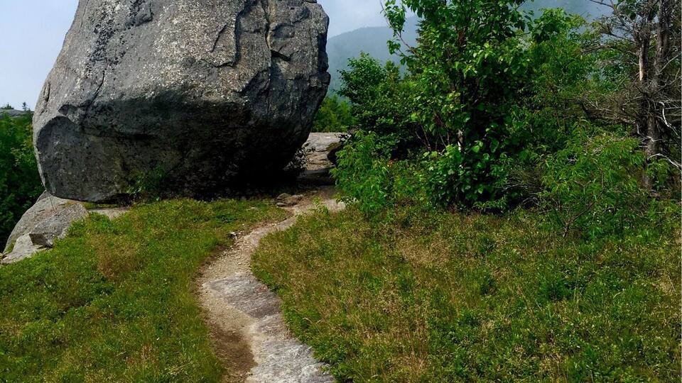 A large rock formation with a narrow path leading through a grassy area.
