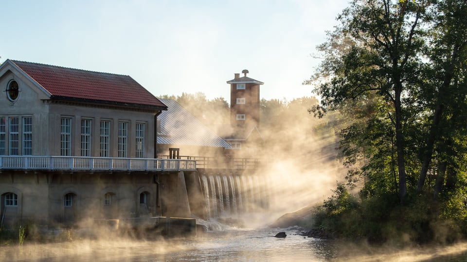 A historic building with a red roof, a water dam, and a tower.