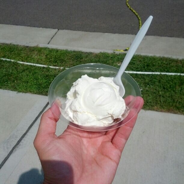 A hand holding a plastic cup with a white substance, possibly ice cream, and a white plastic spoon.