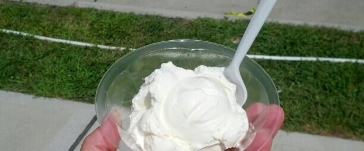 A hand holding a plastic cup with a white substance, possibly ice cream, and a white plastic spoon.