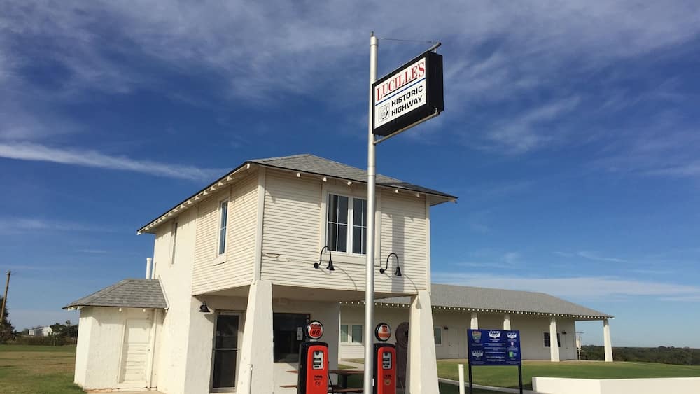 A white building with a sign for Lucille's Historic Highway. There are two red gas pumps in front.