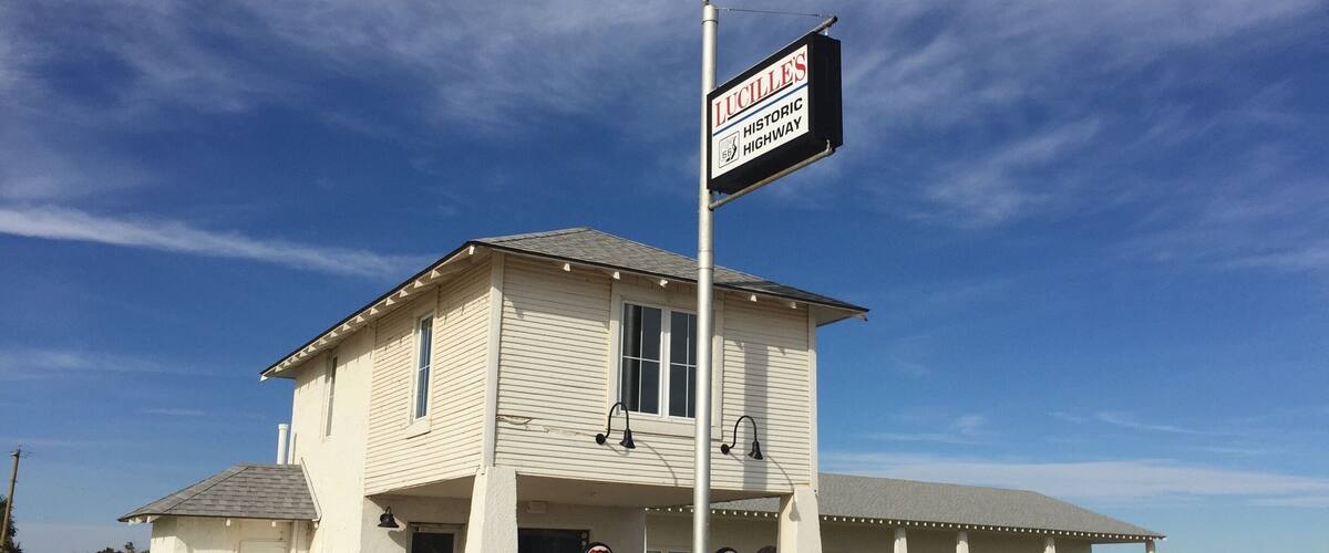 A white building with a sign for Lucille's Historic Highway. There are two red gas pumps in front.