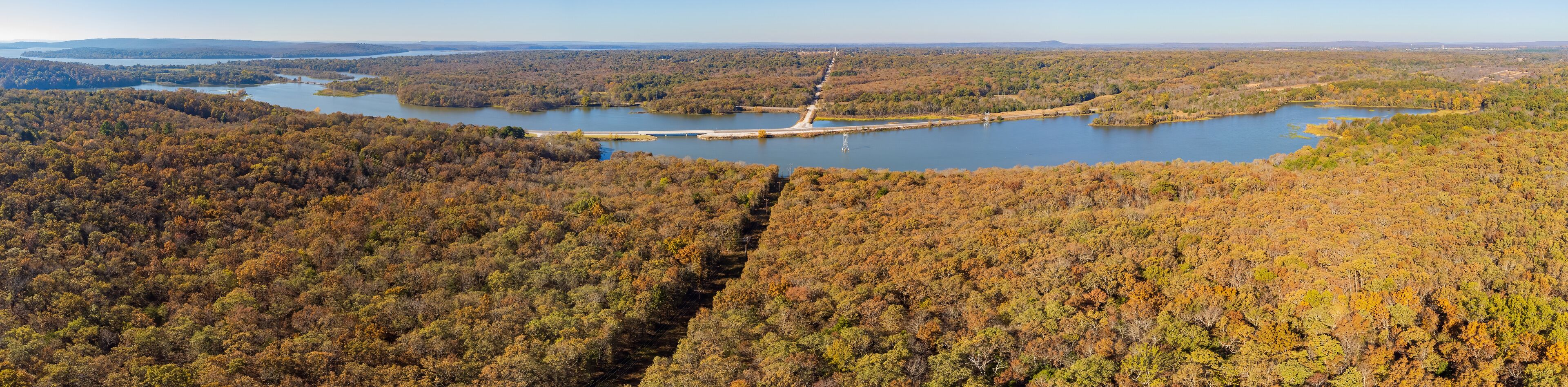 A river winding through a forested valley with a dam and power lines.