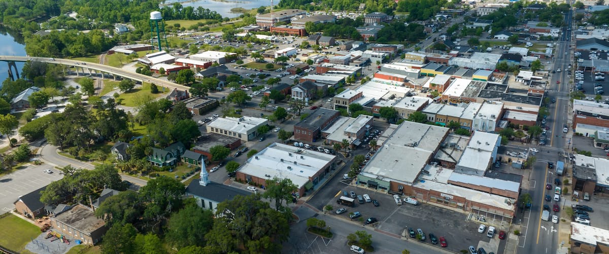 An aerial view of a town with a river, a bridge, and various buildings.