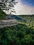 A rocky cliff overlooking a dense forest with a clear sky.