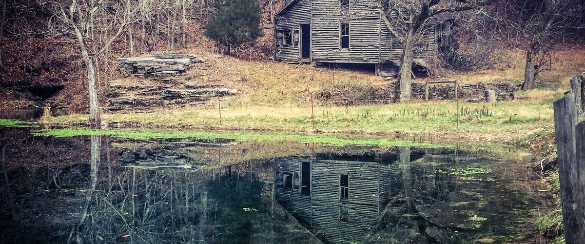 A rustic cabin surrounded by a forest and a calm pond.