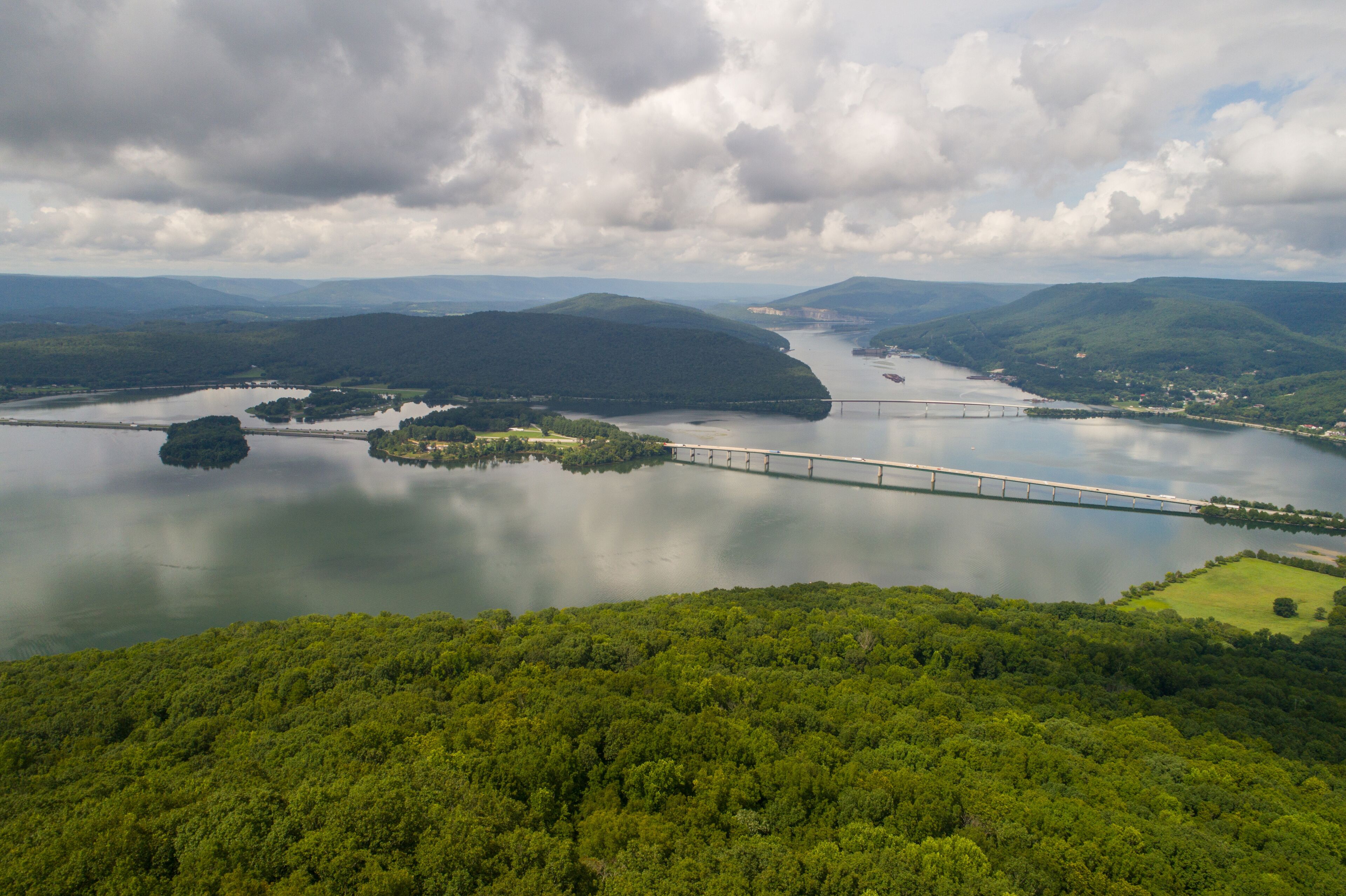 A bridge over a river with surrounding hills and a cloudy sky.
