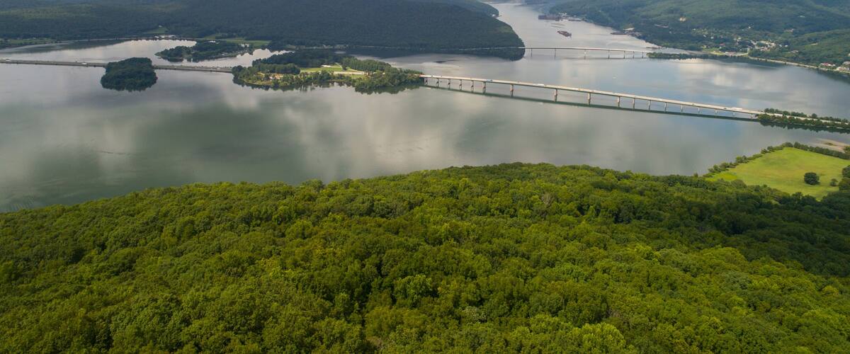 A bridge over a river with surrounding hills and a cloudy sky.