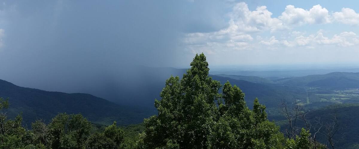 A mountainous landscape with dense green forests and a cloudy sky.