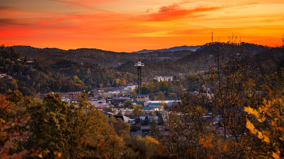 A town nestled in a valley with autumn foliage, surrounded by hills and a sunset sky.