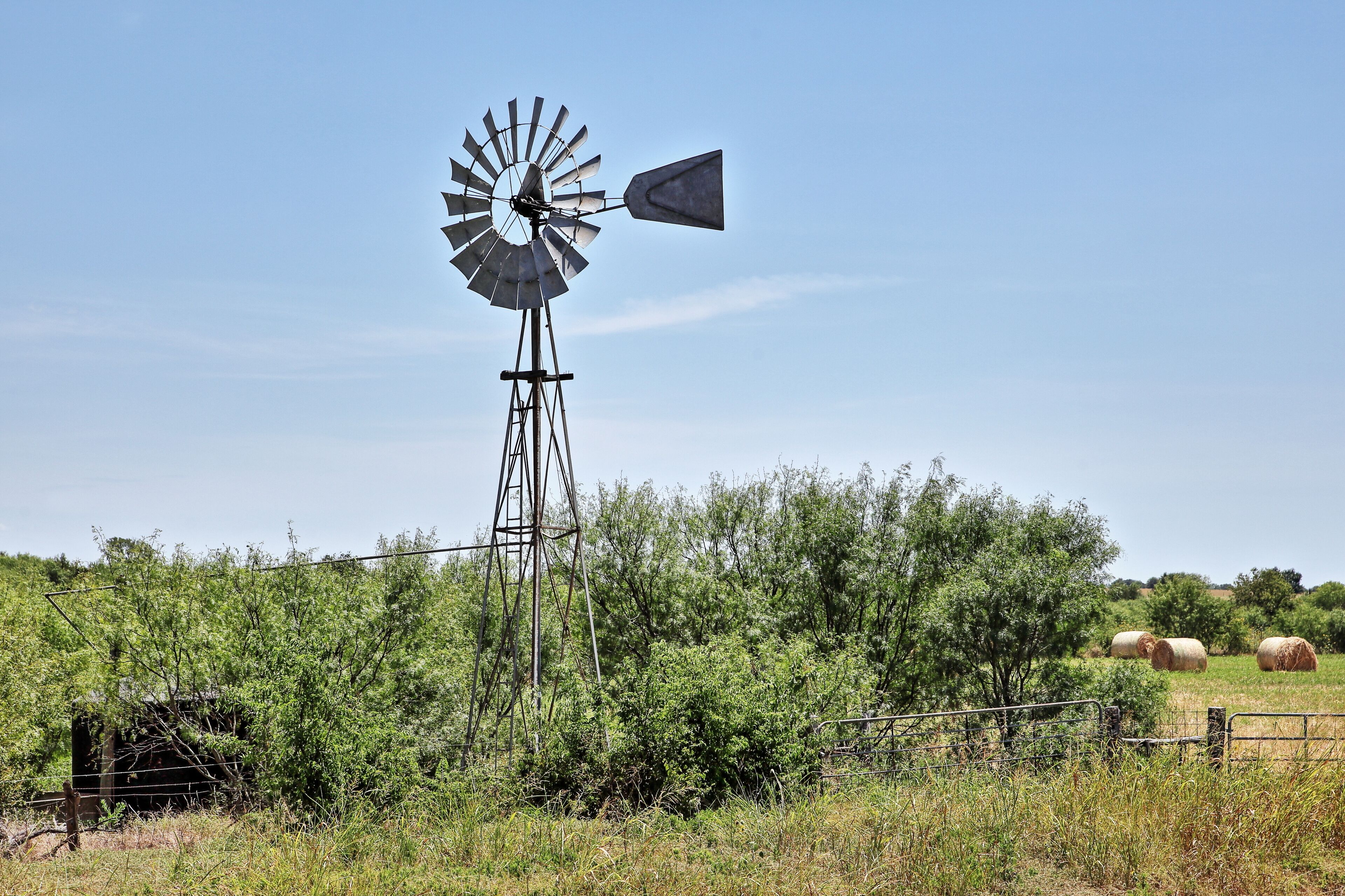 A windmill in a rural landscape with hay bales and sparse vegetation.