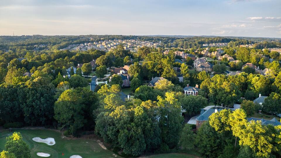 A residential area with houses surrounded by dense trees and a golf course.