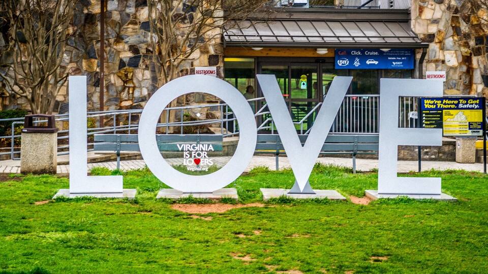 A large LOVE sign in front of a building with a stone facade and a sign that reads "Virginia is for Lovers."