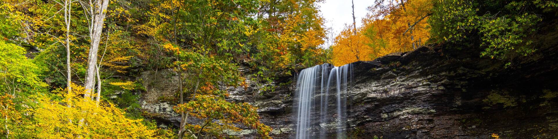 A multi-tiered waterfall cascading into a calm pool surrounded by autumn foliage.
