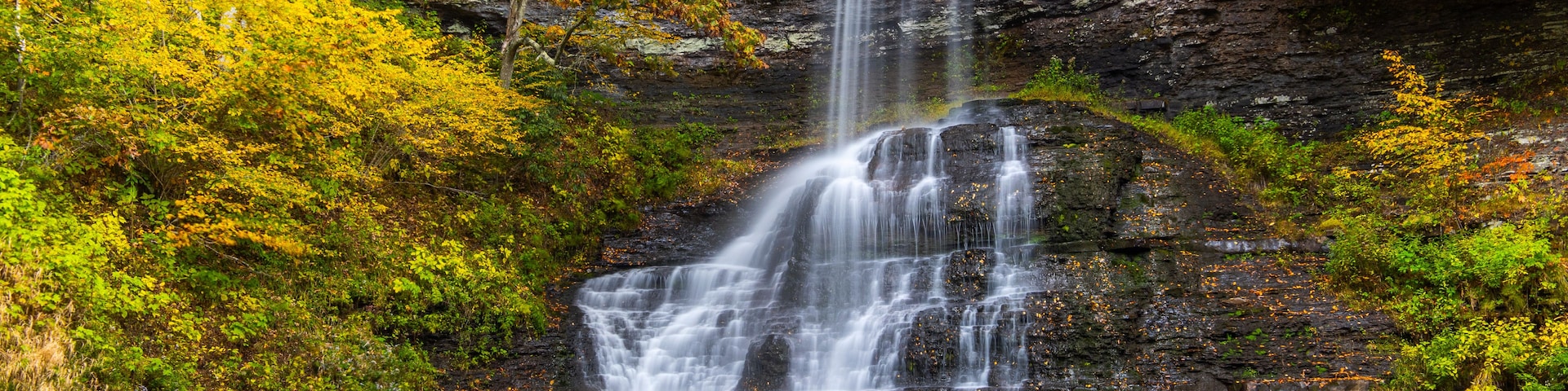 A multi-tiered waterfall cascading into a calm pool surrounded by autumn foliage.