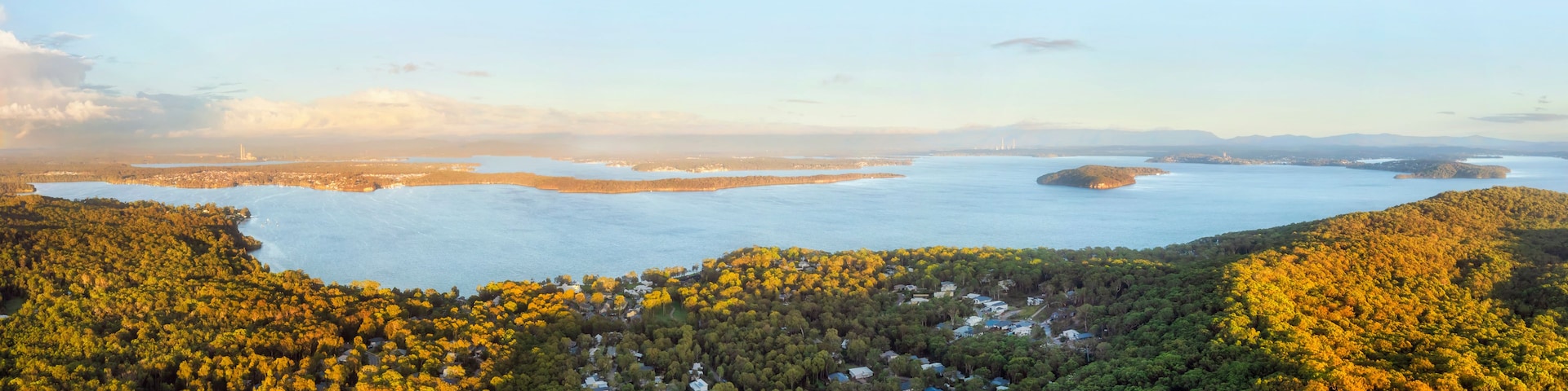 Paisagem costeira com colinas arborizadas, uma grande massa de água e o horizonte de uma cidade ao longe.