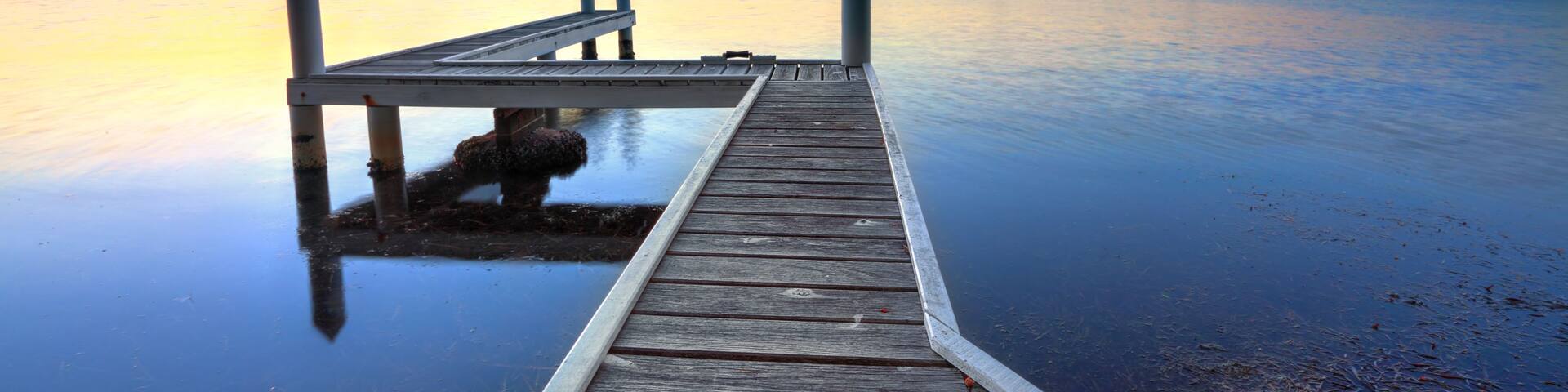 A wooden pier extending into calm water with a sunset in the background.