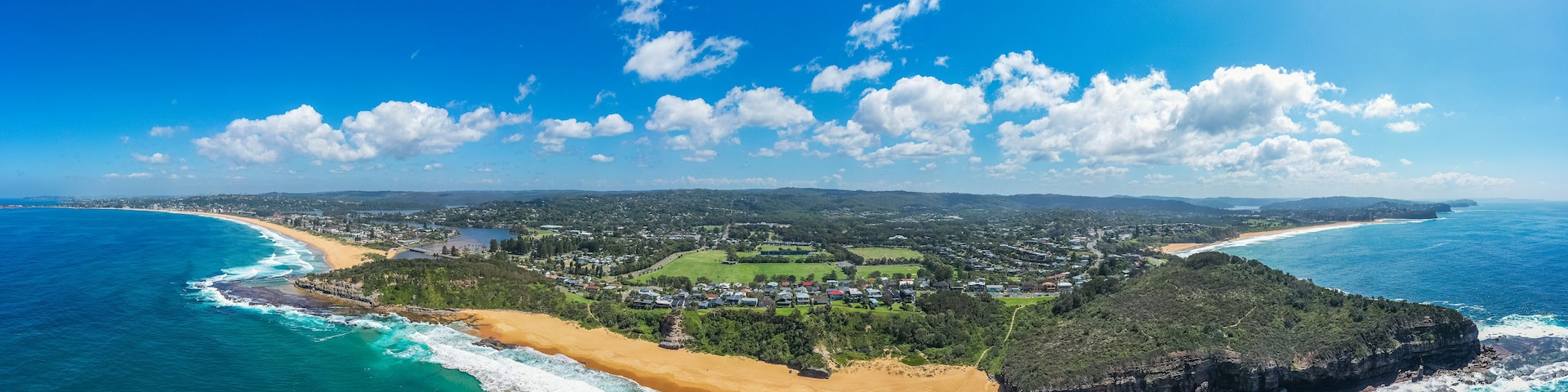 Uma cidade costeira com praia, oceano e colinas ao redor.